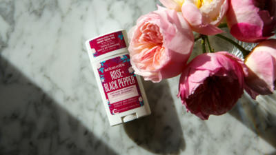 Schmidt's Rose+Black Pepper hemp seed oil deodorant on a marble countertop next to pink flowers
